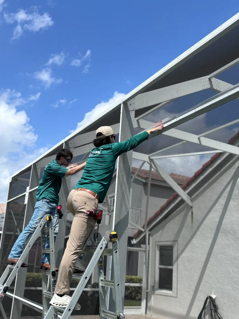 Two technicians working on a lanai screen enclosure in South Florida, focusing on iguana prevention and property protection.